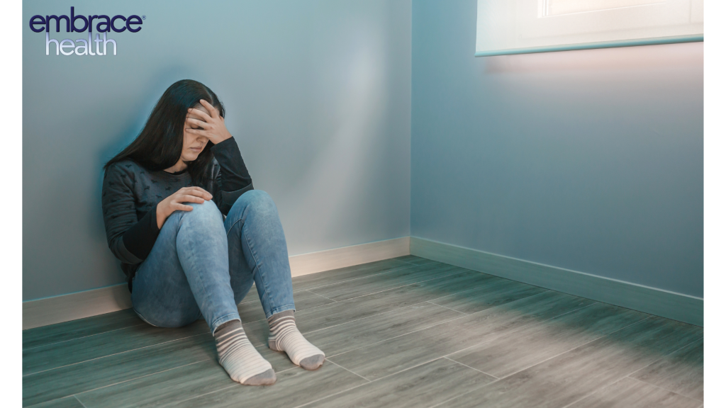A woman sitting on the floor with her head in her hands, showing signs of burnout, fatigue, and the mental health challenges many adults face in balancing work, life, and personal well-being.